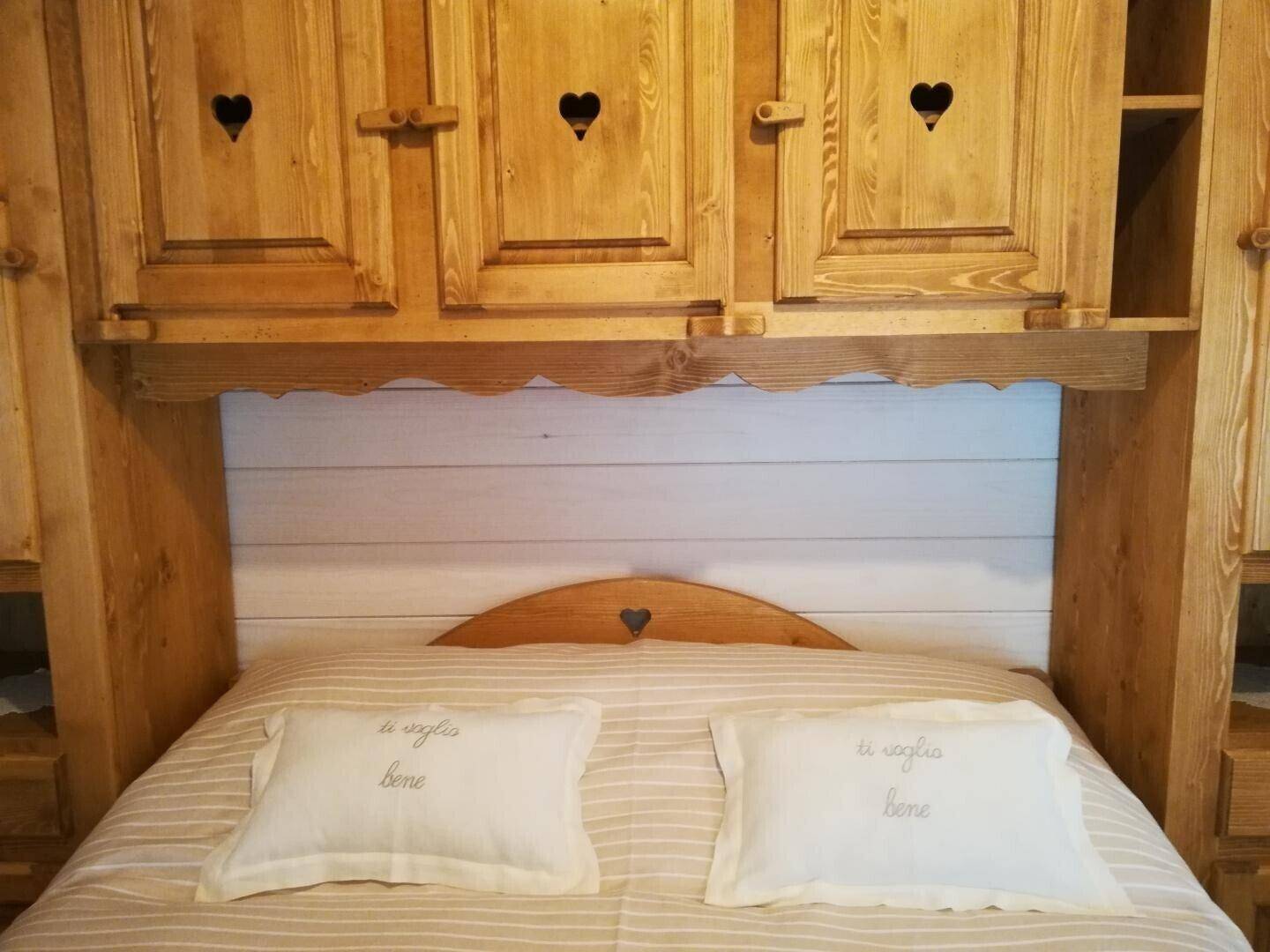 Detailansicht des Bettes mit geschnitztem Kopfteil und integrierten Holzschränken im Schlafzimmer.