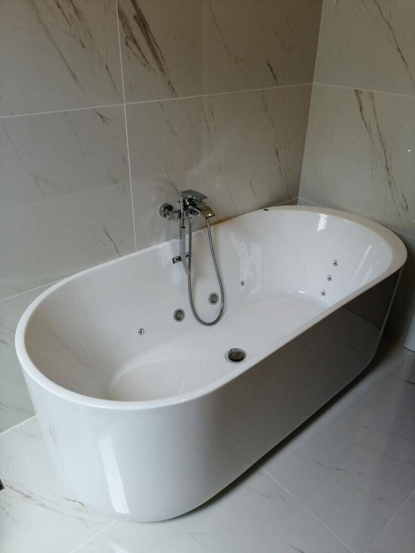 Freistehende Badewanne mit Whirlpool-Funktion in einem modernen Badezimmer mit hellen Fliesen.
