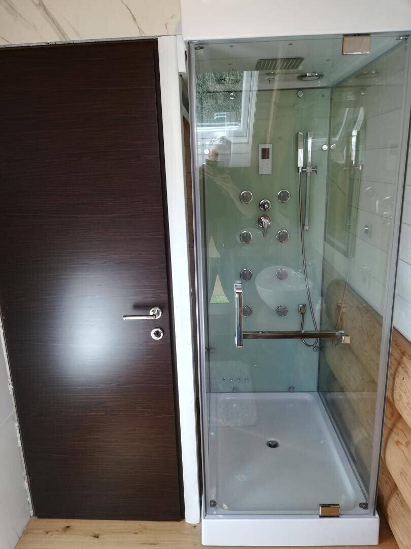 Moderne Duschkabine mit Glaswänden und Massagedüsen neben einer dunklen Holztür.