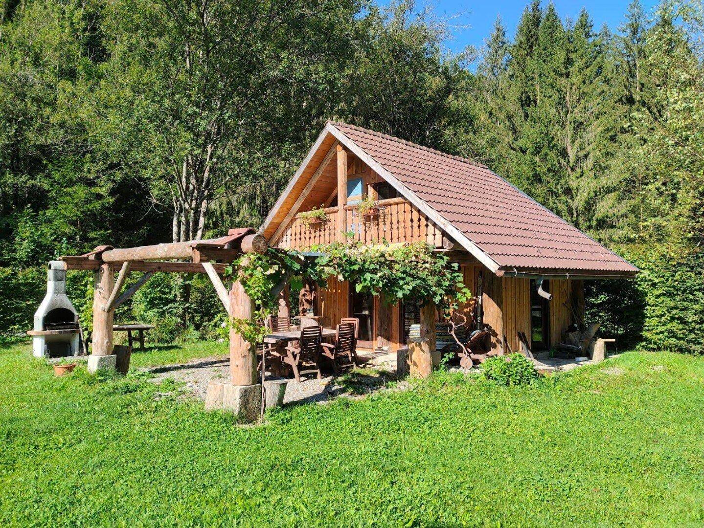 Kleines Holzhaus mit überdachtem Essbereich im Freien und Grillstelle in sonniger Umgebung.