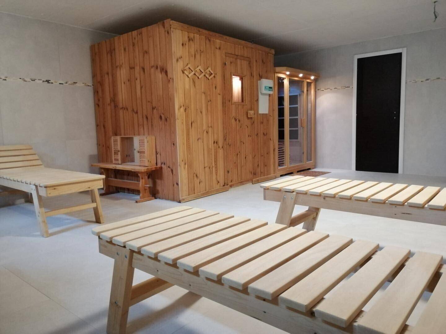 Geräumiger Wellnessbereich mit Holzsauna, Infrarotkabine und Liegestühlen für Entspannung.