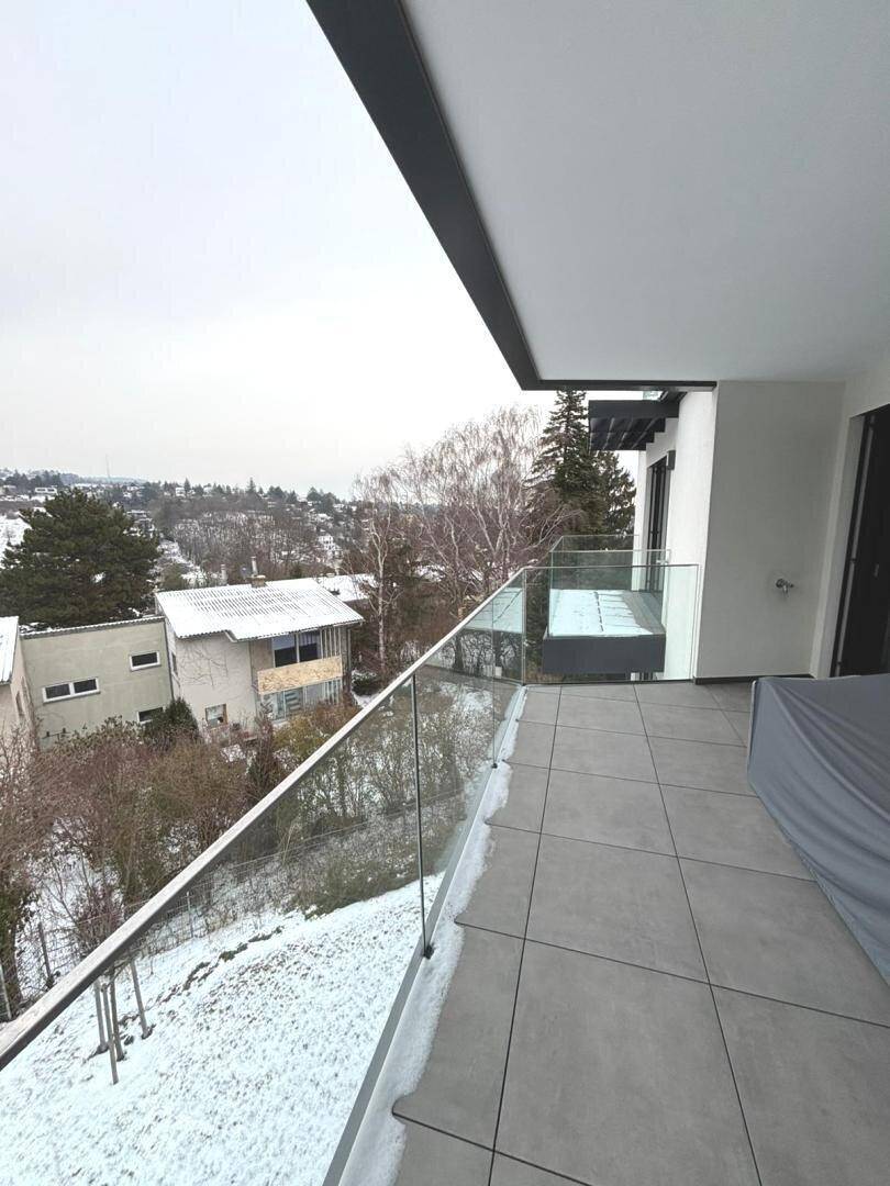 Schneebedeckter Balkon mit Glasgeländer und winterlichem Ausblick auf die Umgebung.