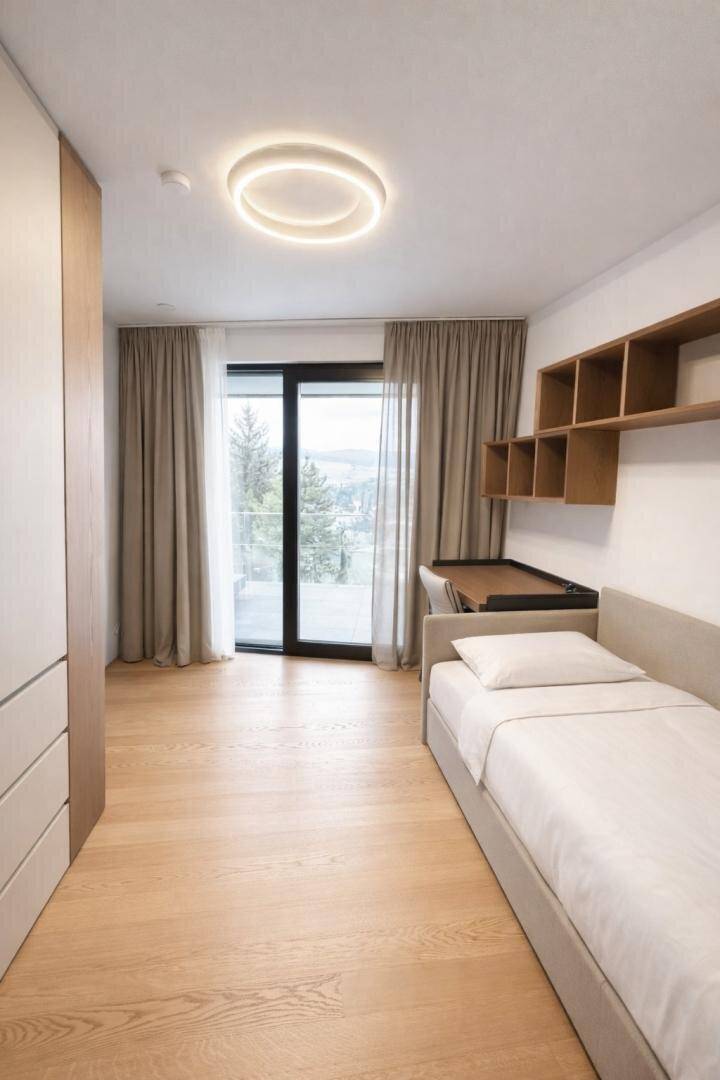 Schlafzimmer mit Einzelbett, Schreibtisch und großem Fenster mit Zugang zum Balkon und Aussicht.