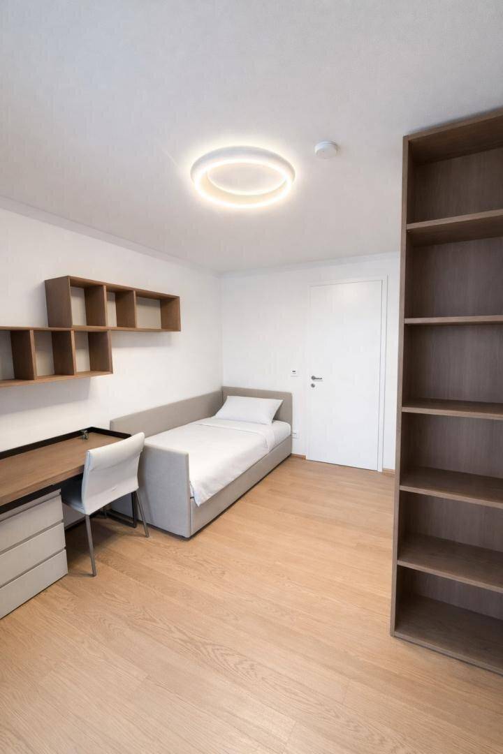 Helles Schlafzimmer mit Einzelbett, Schreibtisch und praktischen Holzregalen.