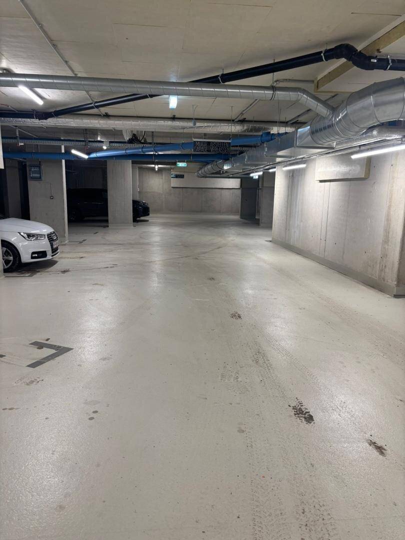 Geräumige Tiefgarage mit Betonwänden, sichtbaren Leitungen und ausreichend Stellplätzen.