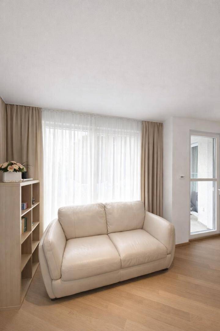 Gemütliches Wohnzimmer mit hellem Sofa, Holzboden und Zugang zum Balkon.