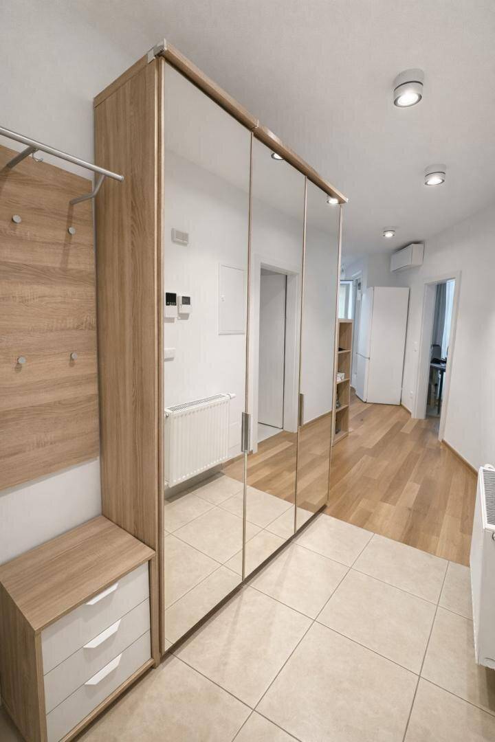 Heller Flur mit Spiegelschränken, Holzboden und Fliesen im Eingangsbereich.