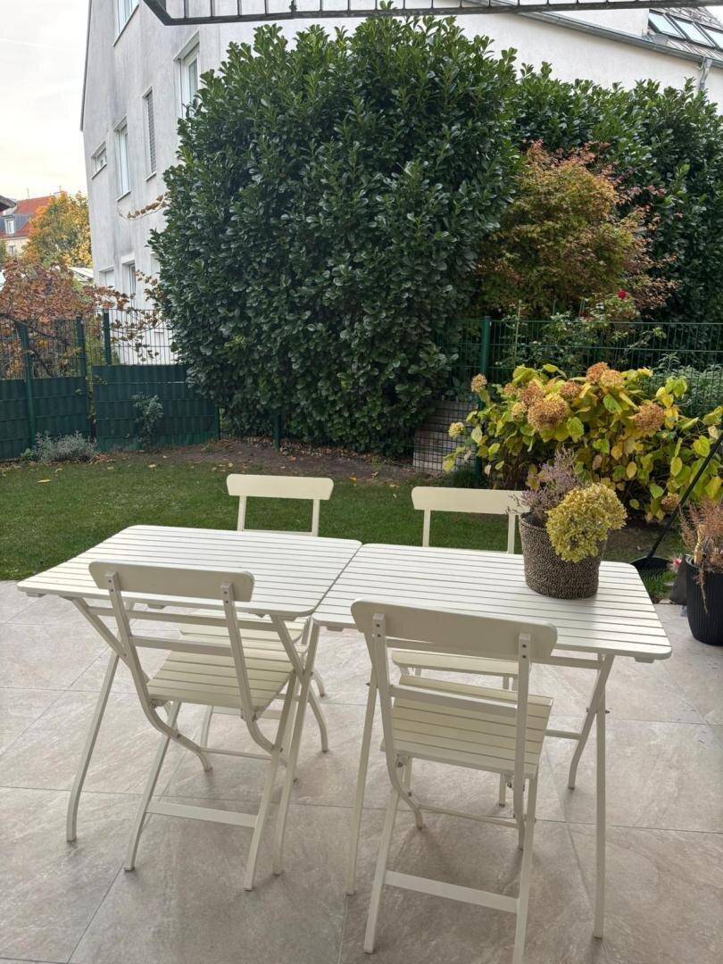 Gemütliche Terrasse mit Gartenmöbeln, Fliesenboden und Blick ins Grüne.