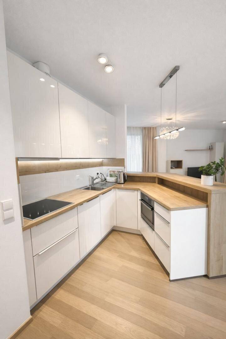 Moderne Einbauküche mit weißen Hochglanzfronten, Holz-Arbeitsplatten und Induktionskochfeld.