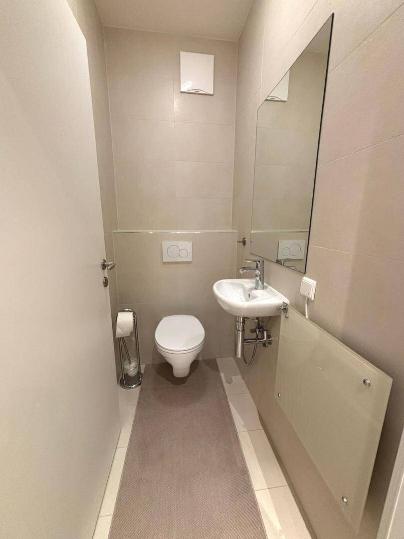 Modernes Gäste-WC mit wandhängendem WC, kleinem Waschbecken und Spiegel.