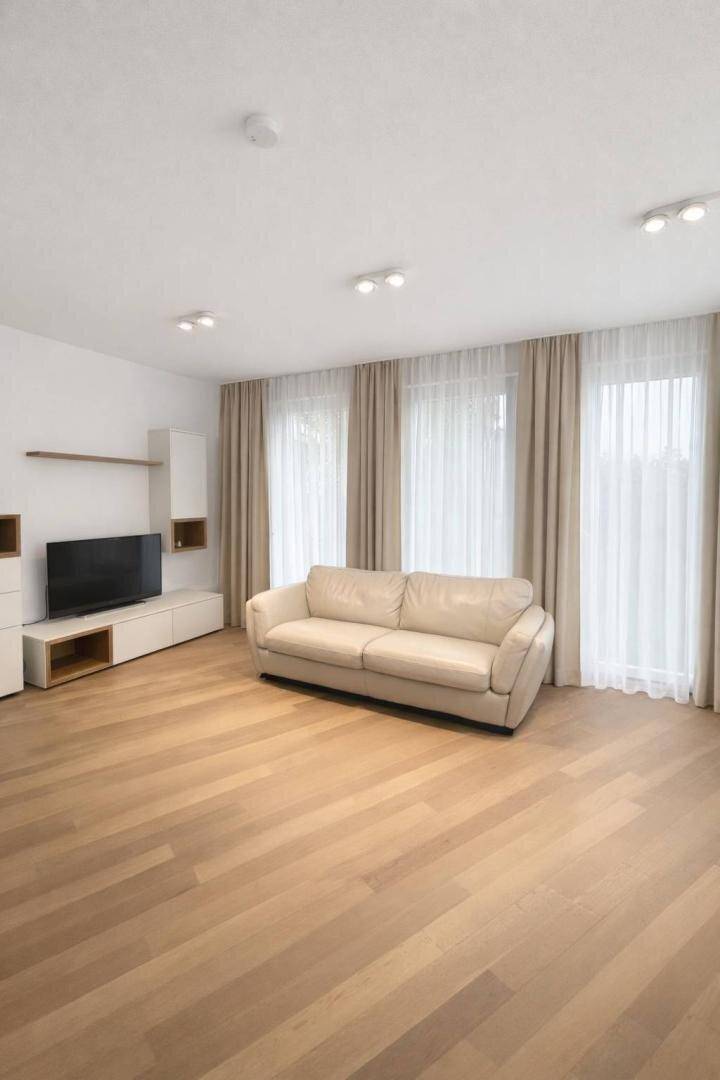 Geräumiges Wohnzimmer mit hellem Sofa, Holzboden und großen Fenstern.