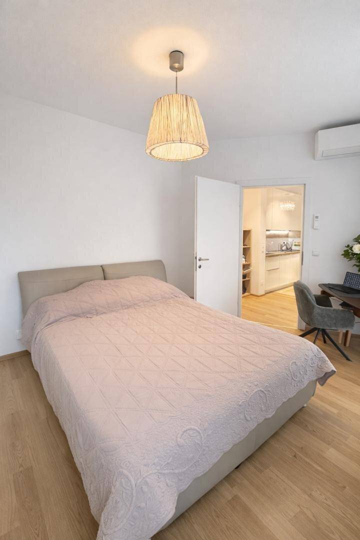 Helles Schlafzimmer mit Doppelbett, Holzboden und Blick in die offene Küche.
