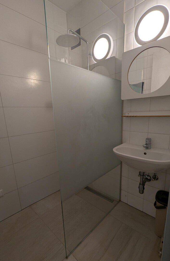Modernes Badezimmer mit begehbarer Dusche, Waschbecken und runden Fenstern.