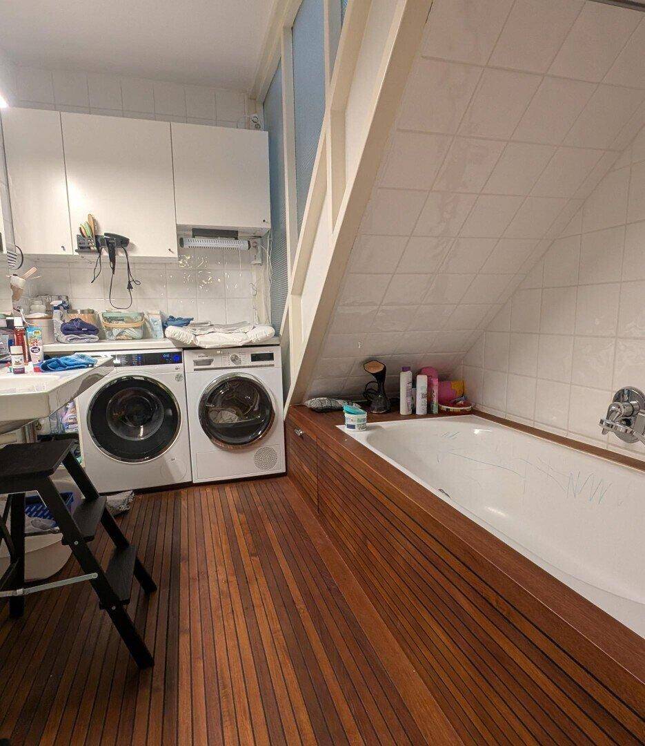Badezimmer mit Badewanne, Waschmaschinen und Holzboden unter Dachschräge.