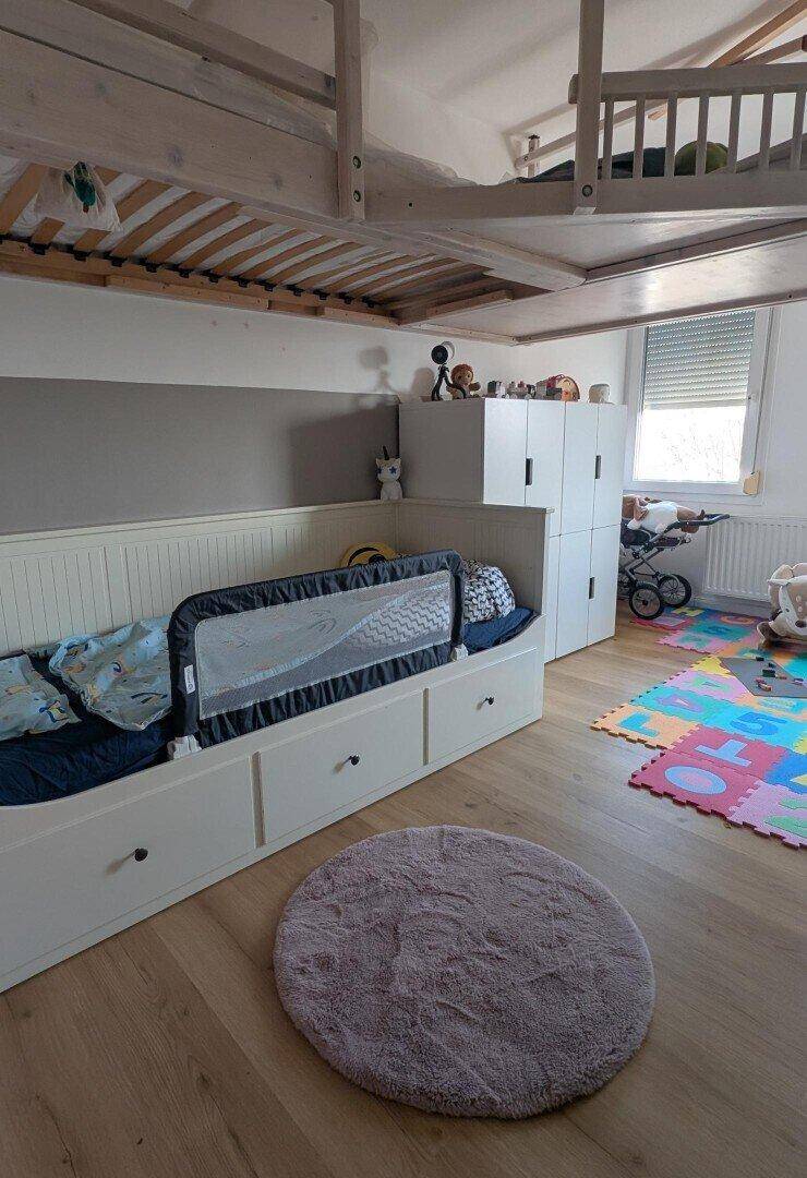 Kinderzimmer mit Holzboden, Spielteppich und einem Hochbett über dem Bett.