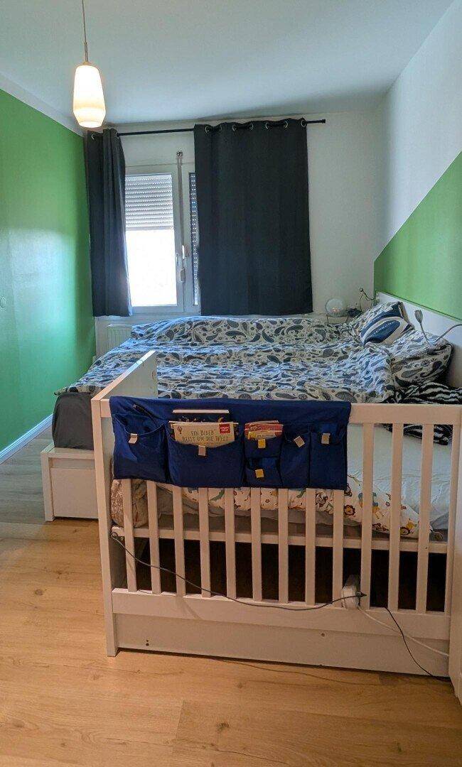 Schlafzimmer mit Doppelbett, Babybett und grüner Akzentwand.