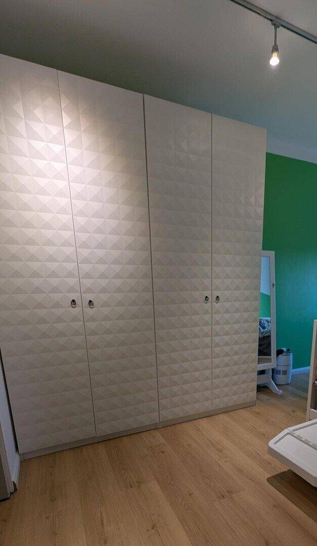 Schlafzimmer mit großem weißen Kleiderschrank und Holzboden.