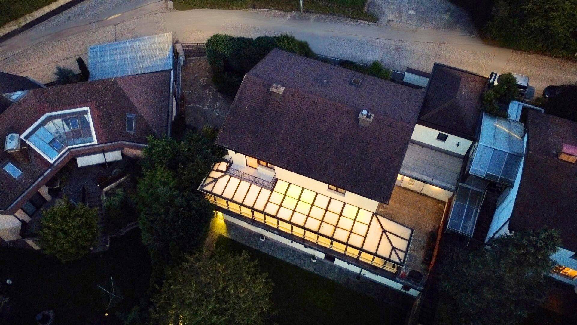 Luftaufnahme des Hauses und der Nachbarschaft bei Dämmerung mit beleuchteter Terrasse.