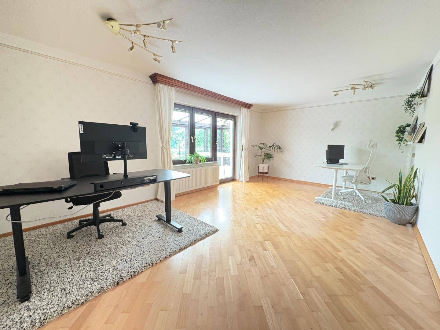 Geräumiges Büro mit zwei Arbeitsplätzen, Holzboden und Blick zum Wintergarten.