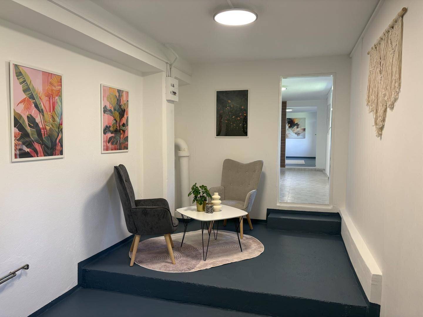 Heller Flurbereich mit Sitzgelegenheiten, moderner Kunst und Zugang zu weiteren Räumen.