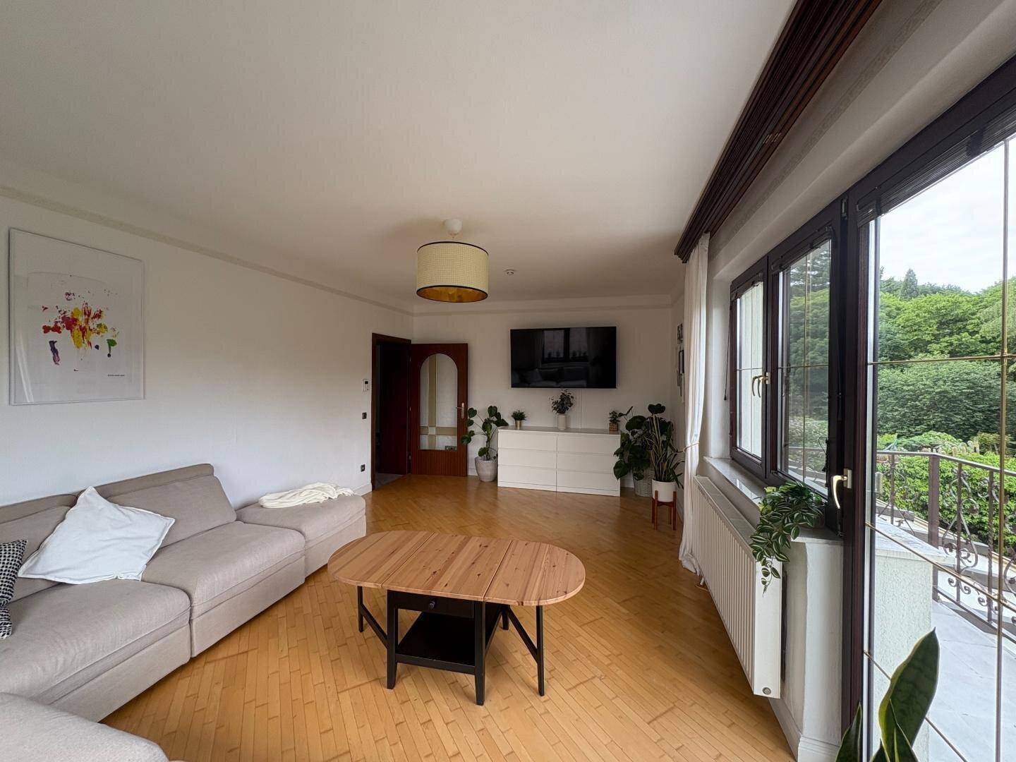 Wohnzimmer mit Holzboden, Sofa, Fernseher und Zugang zu einem Balkon.