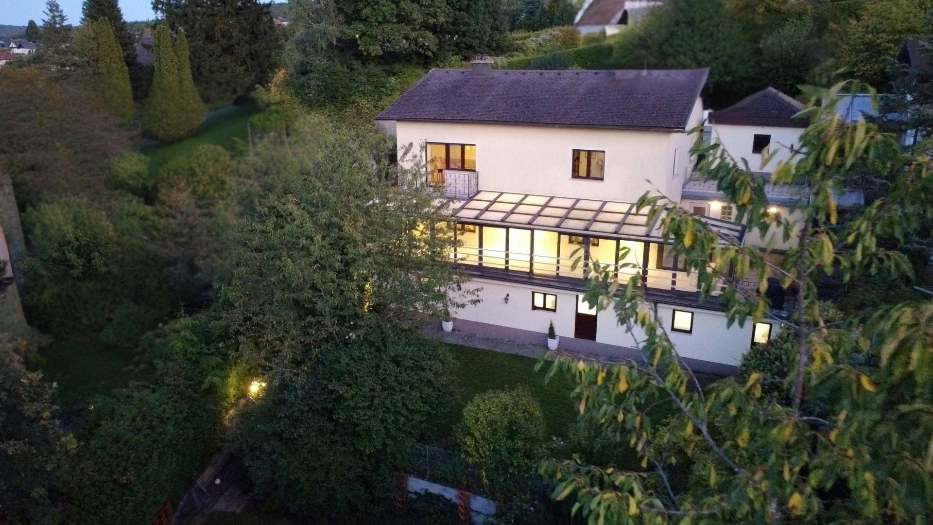 Luftaufnahme des Hauses umgeben von üppiger grüner Landschaft bei Einbruch der Dämmerung.