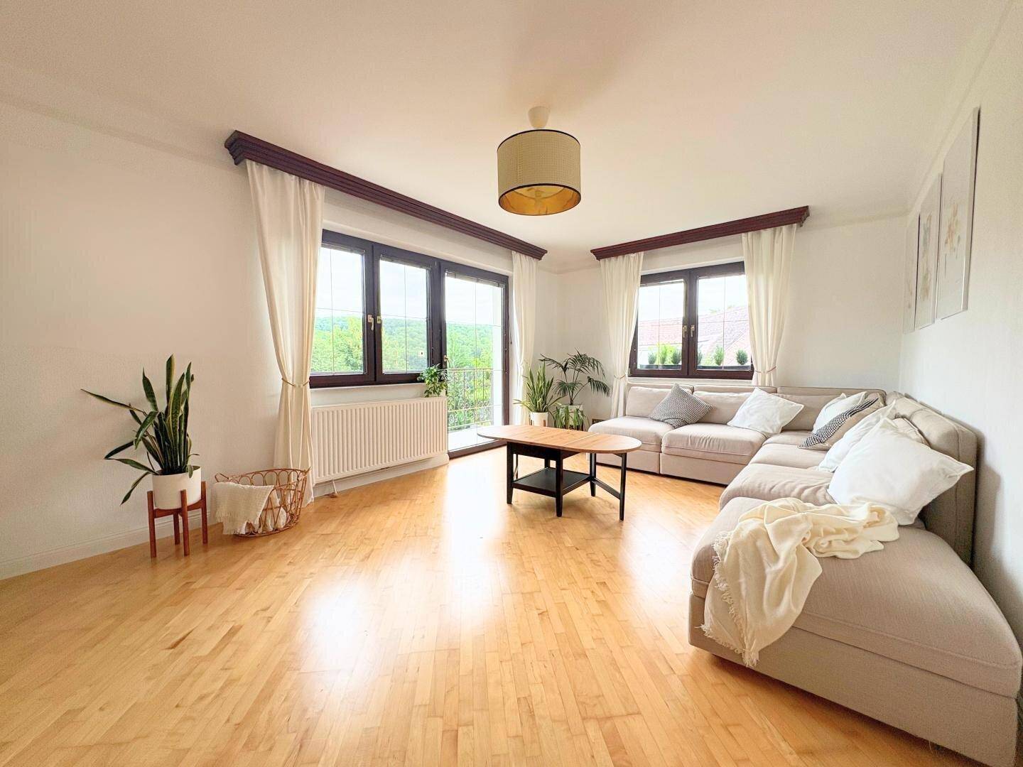 Helles Wohnzimmer mit hellem Holzboden, großem Sofa und Blick ins Grüne.