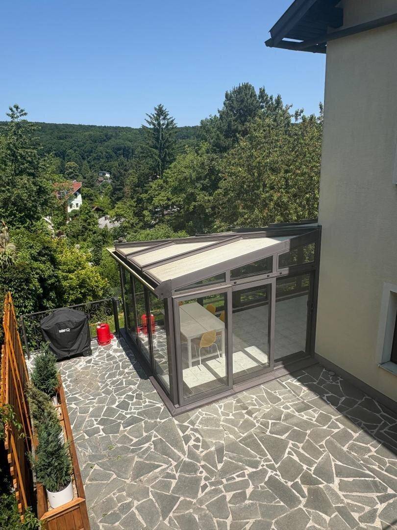 Sonnenterrasse mit Steinplatten, verglastem Essbereich und Grillstation.