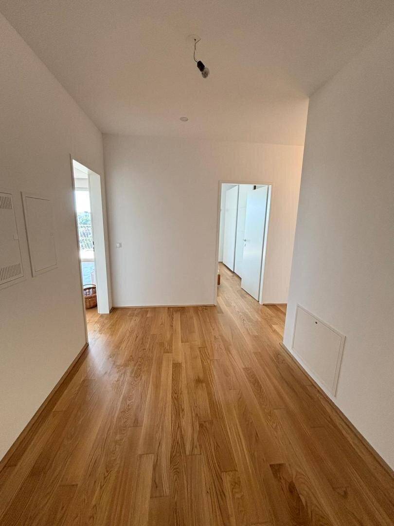 Leerer Flur mit hellem Holzboden und weißen Wänden, der zu weiteren Räumen führt.