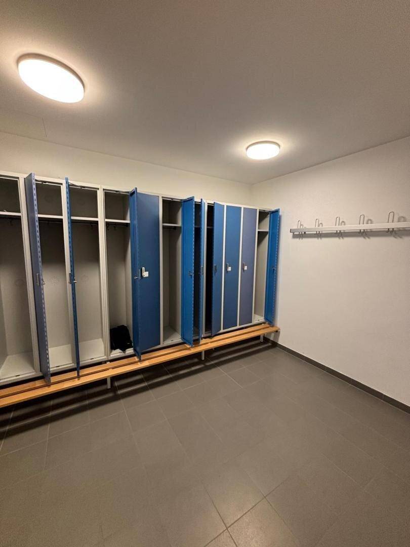 Umkleideraum mit blauen Spinden und Sitzbänken, Teil der Sport- oder Wellnesseinrichtungen.
