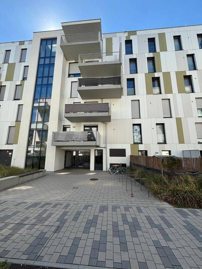 Moderne Wohnhausfassade mit farbigen Paneelen, großen Fenstern und mehreren Balkonen.