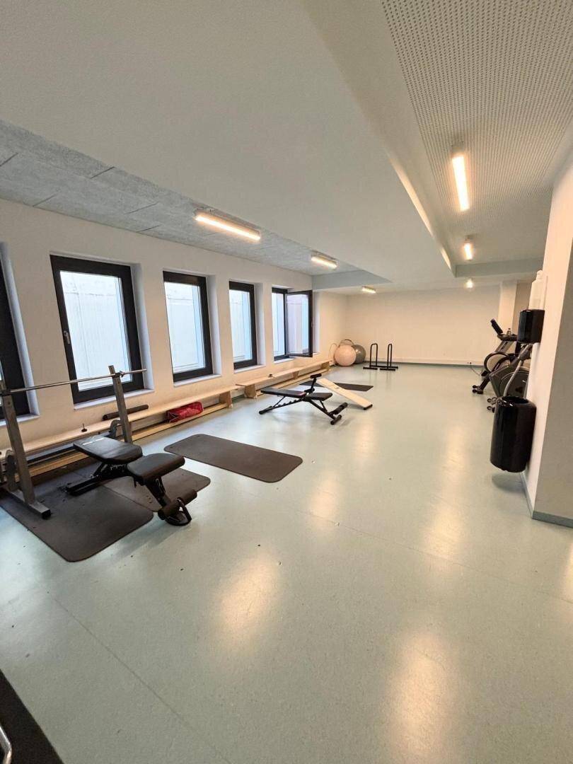 Gut ausgestatteter Fitnessraum mit verschiedenen Trainingsgeräten und Hantelbänken.