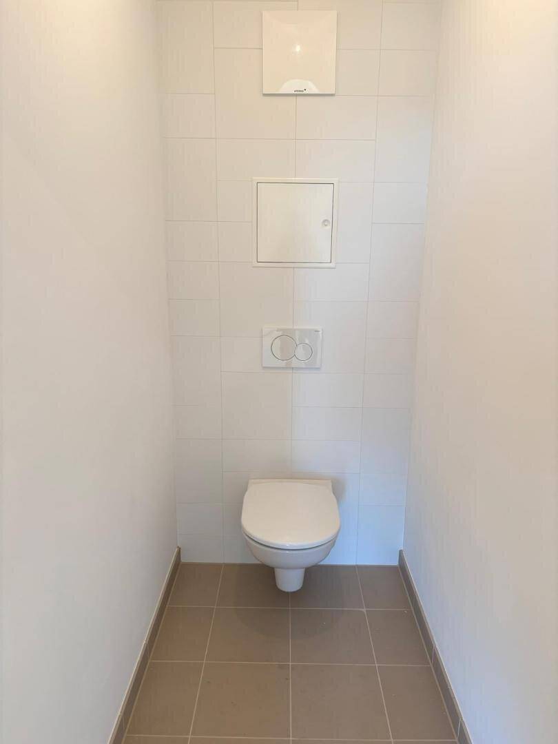 Separates WC mit wandhängender Toilette und hellen Fliesen an Boden und Wänden.