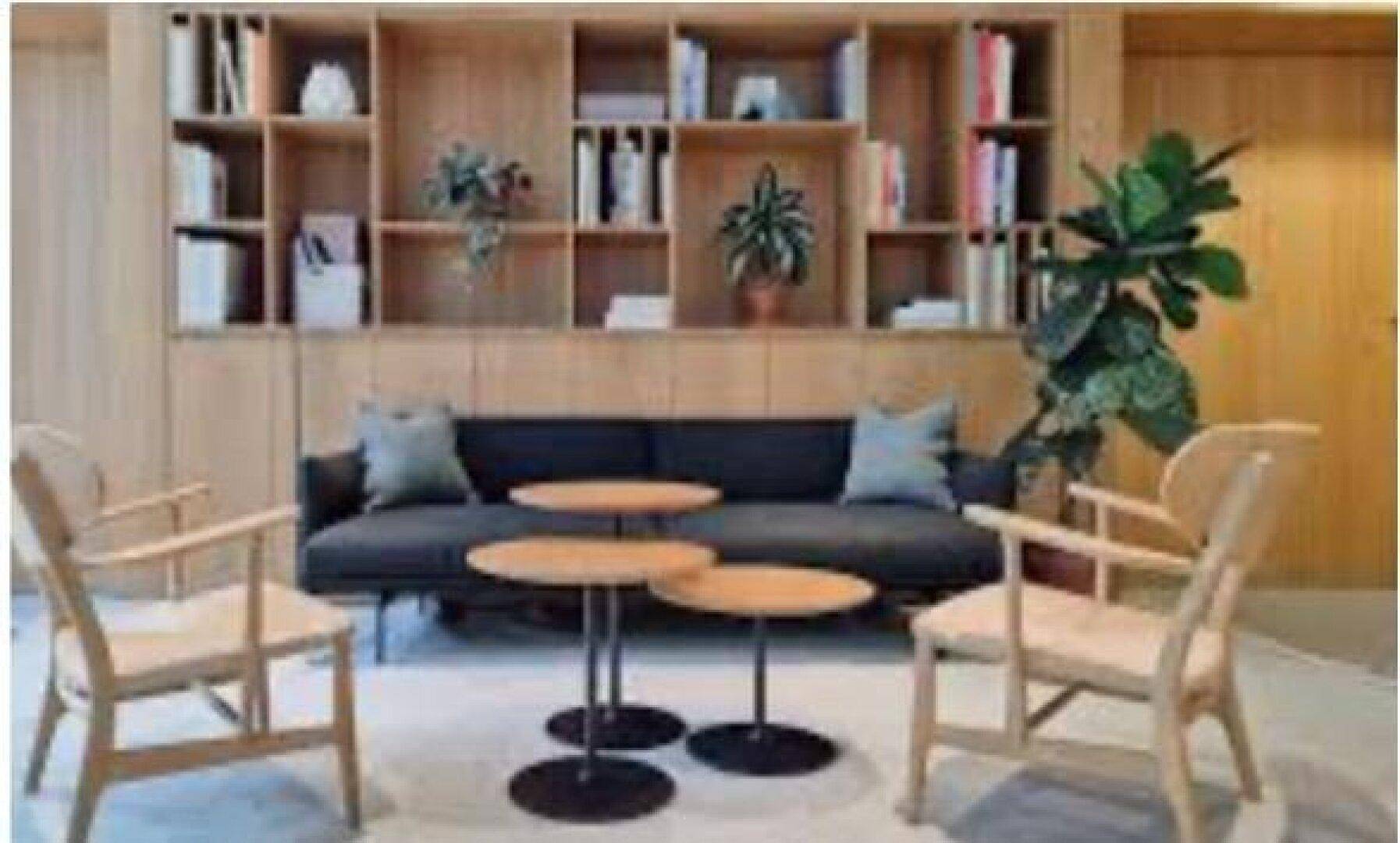 Gemütlicher Loungebereich mit dunklem Sofa, Holzsesseln und einem integrierten Bücherregal.