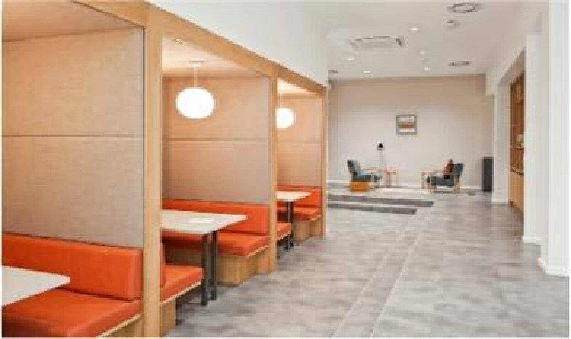 Moderner Bürobereich mit orangefarbenen Sitzkabinen und einem entspannten Loungebereich im Hintergrund.