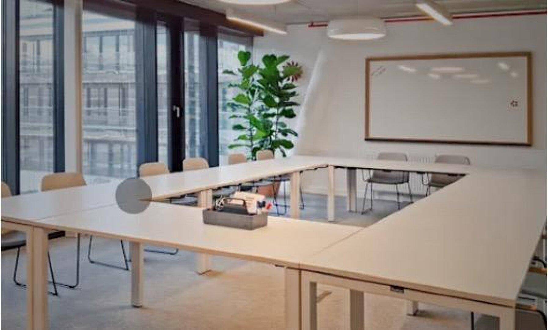 Großer Besprechungsraum mit U-förmiger Tischordnung, großen Fenstern und Whiteboard.