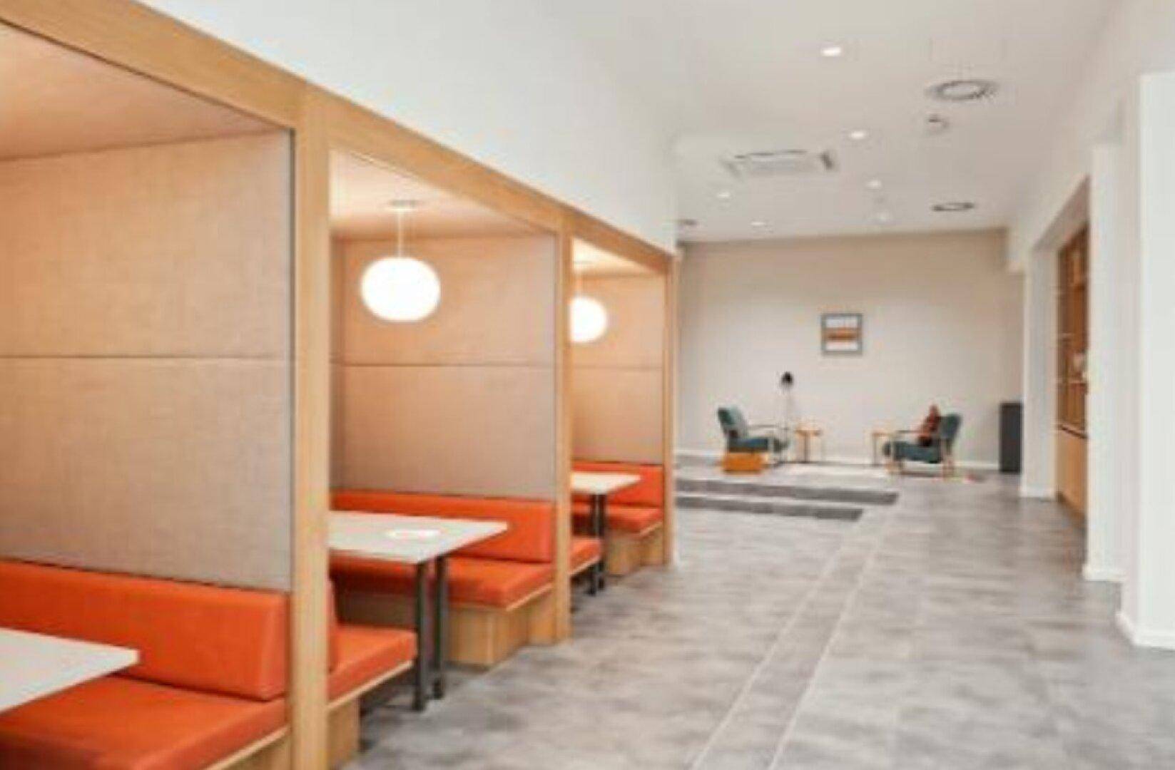 Moderner Bürobereich mit orangefarbenen Sitzkabinen und einem entspannten Lounge-Bereich im Hintergrund.