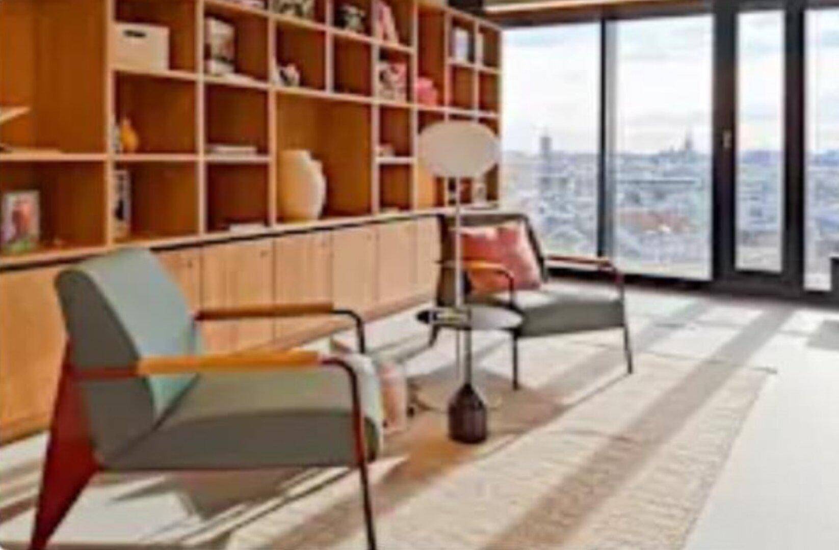 Gemütlicher Wohnbereich mit großem Bücherregal, bequemen Sesseln und Panoramablick auf die Stadt.