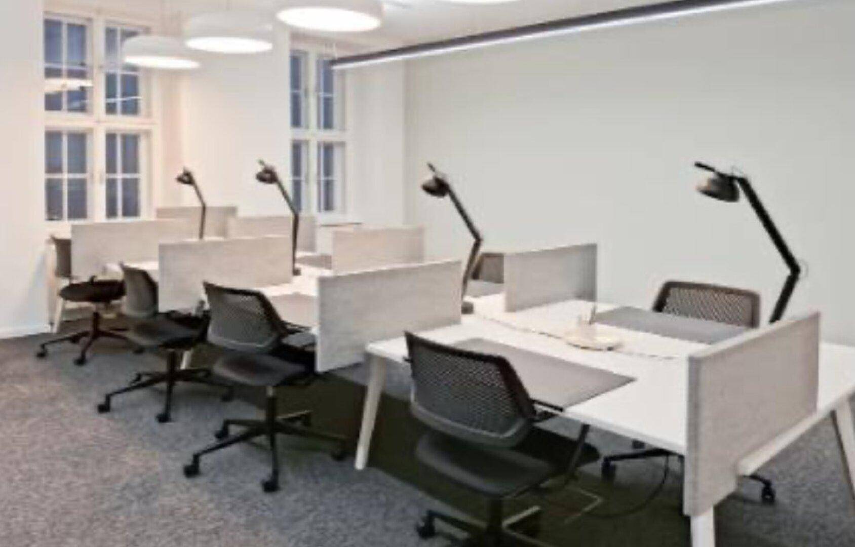 Heller Großraumbüro mit mehreren Arbeitsplätzen, ergonomischen Stühlen und großen Fenstern.