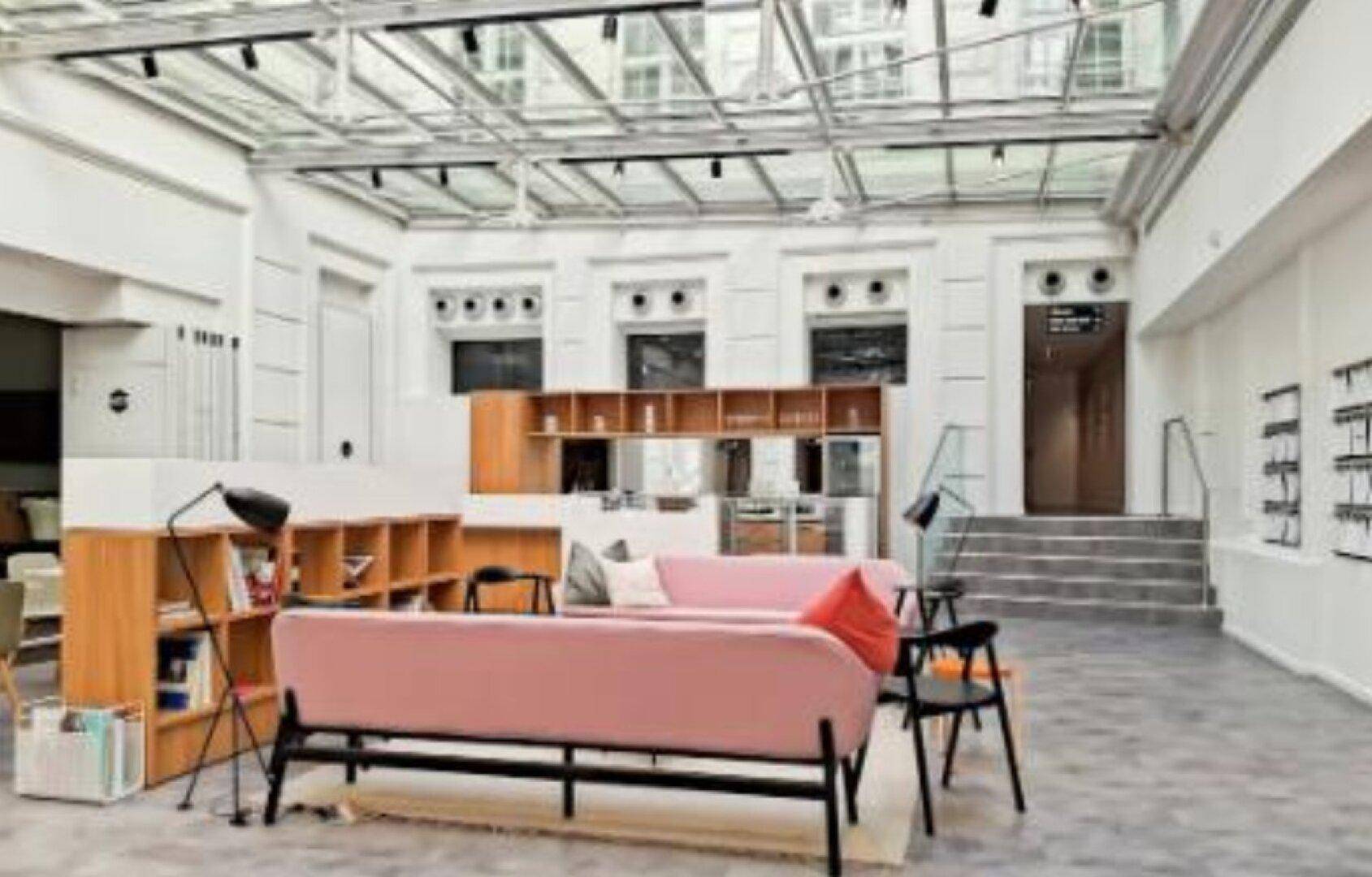 Helle Lobby mit Glasdach, modernen rosa Sofas und Holzregalen, die zum Entspannen einlädt.