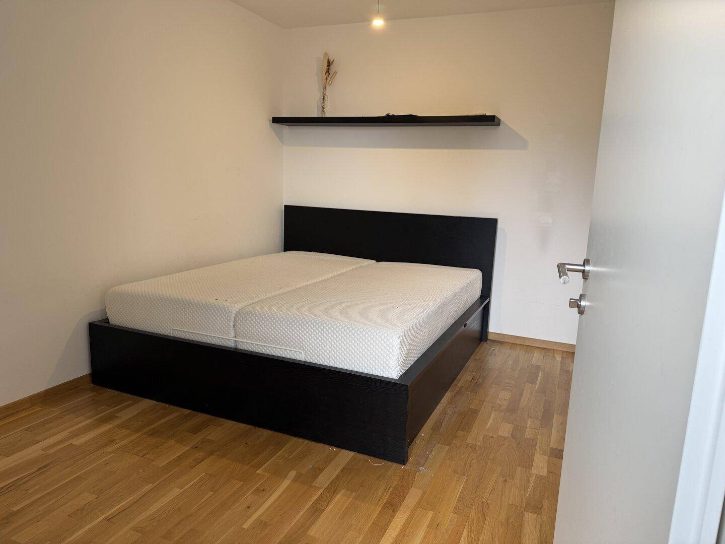 Schlafzimmer mit Doppelbett, Holzboden und schlichter Wanddekoration.