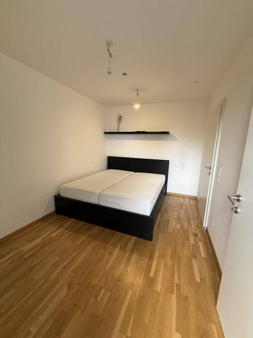 Schlafzimmer mit Holzboden, Doppelbett und schwebendem Wandregal.