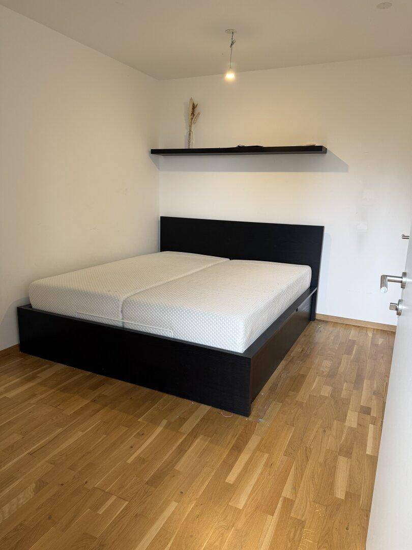 Helles Schlafzimmer mit Holzboden, Doppelbett und minimalistischer Einrichtung.