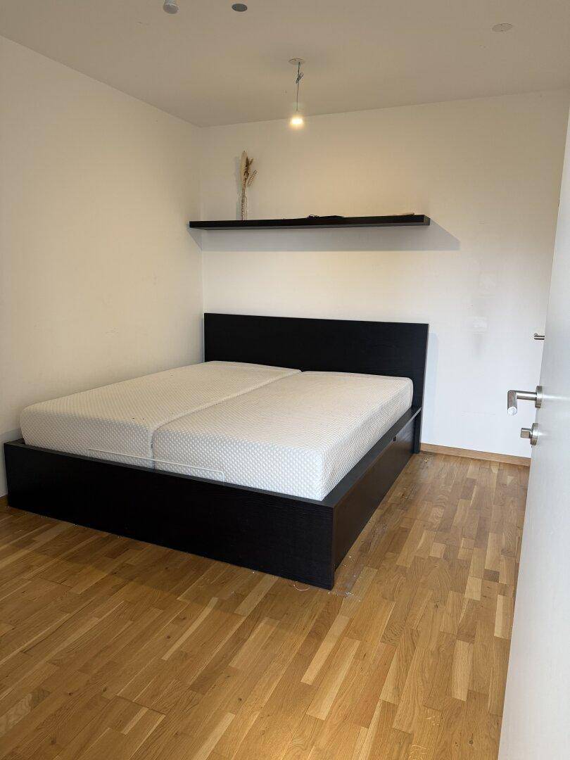 Helles Schlafzimmer mit Holzboden, Doppelbett und einfacher Einrichtung.