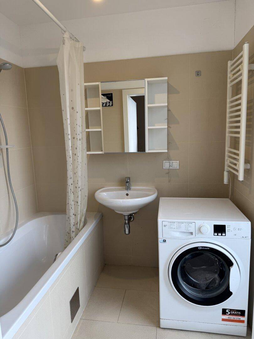 Badezimmer mit Badewanne, Waschbecken, Waschmaschine und beigefarbenen Fliesen.