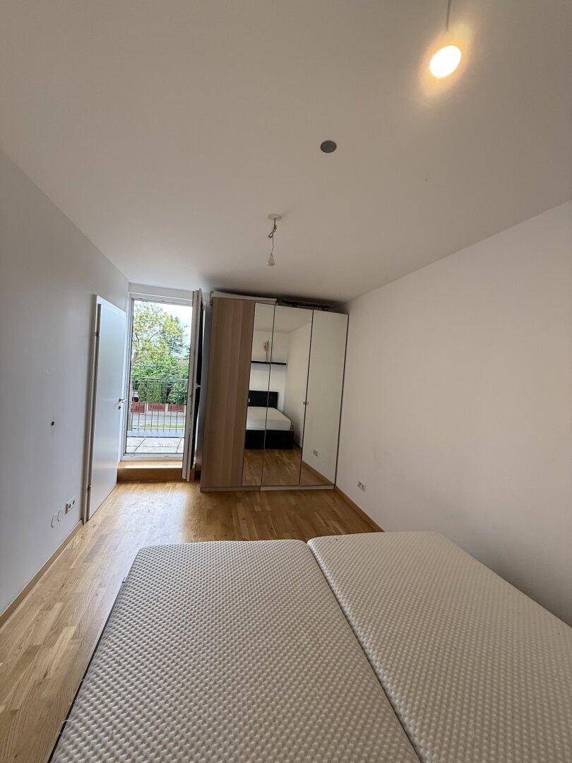 Helles Schlafzimmer mit Holzboden, Spiegelschrank und direktem Balkonzugang.