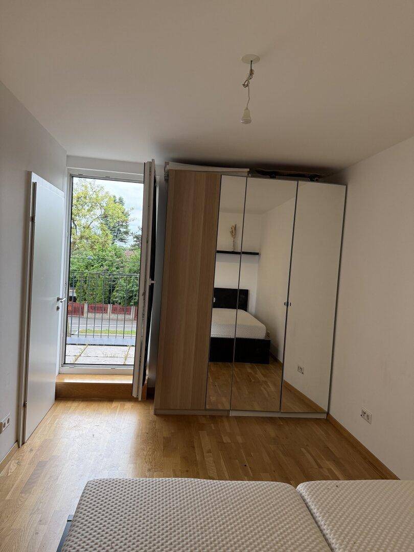 Schlafzimmer mit Holzboden, großem Spiegelschrank und Zugang zu einem Balkon.