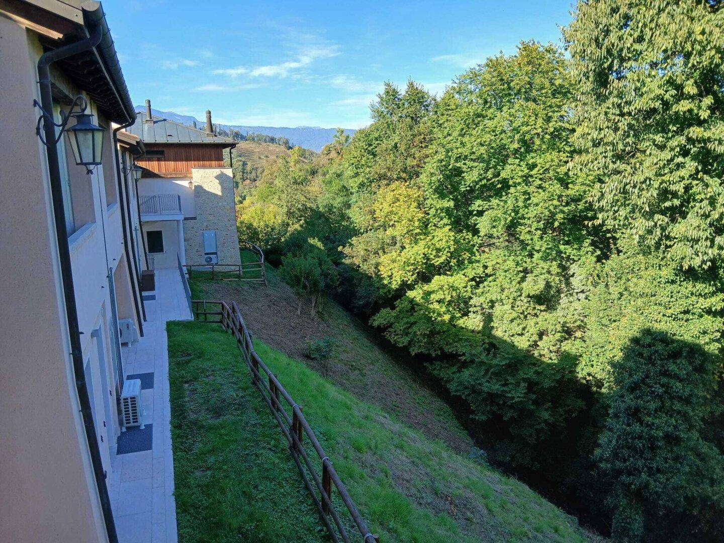 Gebäudeansicht mit Hanglage, umgeben von üppiger grüner Vegetation und Fernblick auf die Berge.