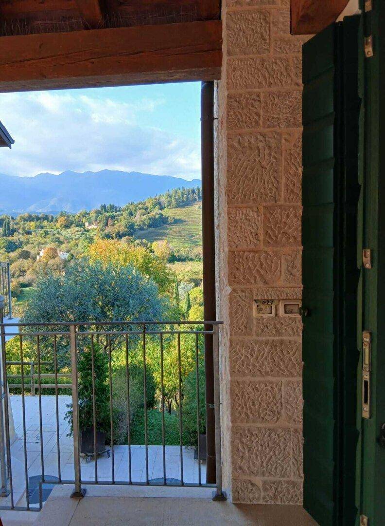 Kleiner Balkon mit Metallgeländer und weitem Blick über grüne Hügel und Berge.