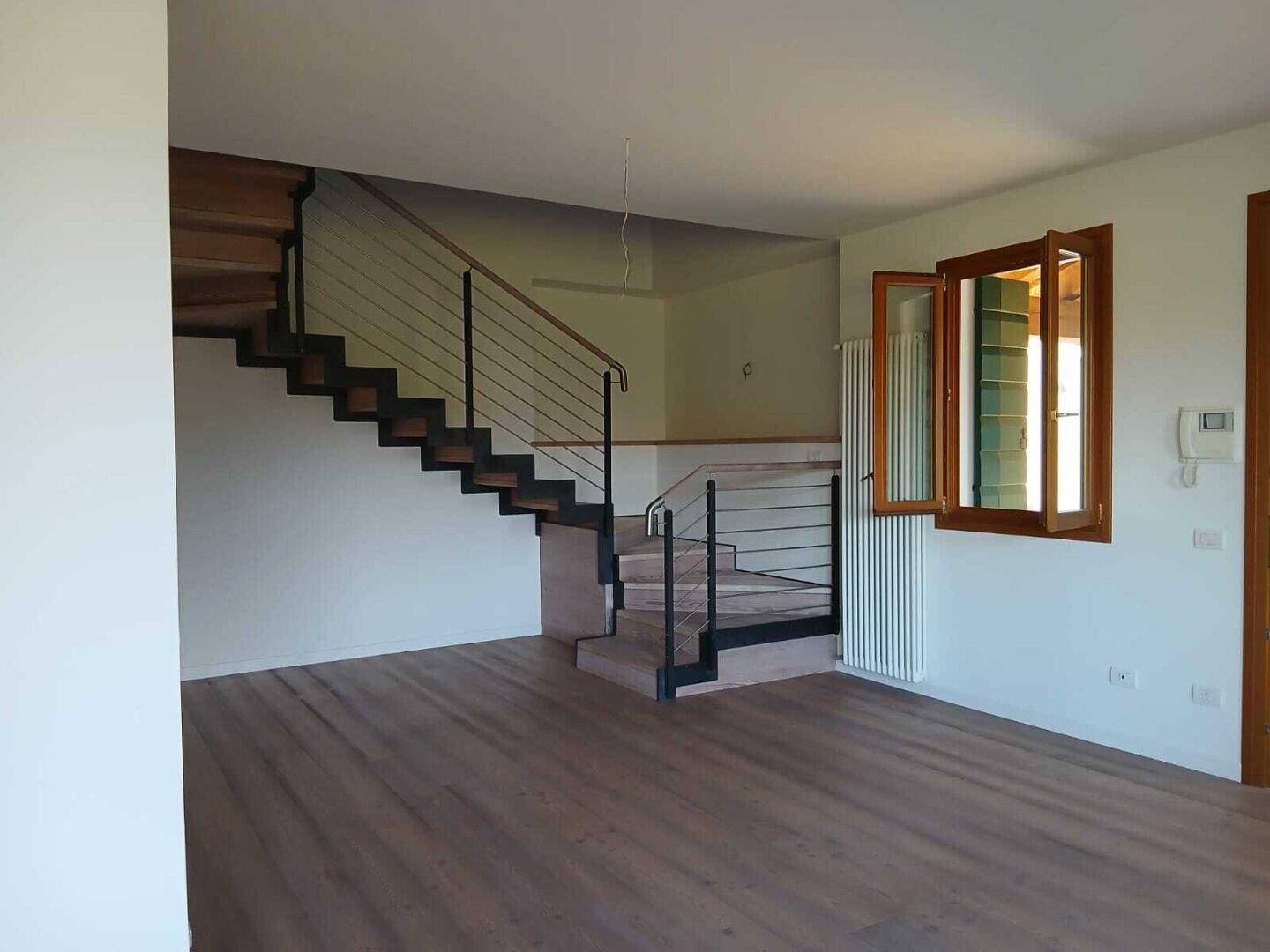 Geräumiger Wohnbereich mit Holzboden, moderner Treppe und Fenster mit Blick ins Grüne.